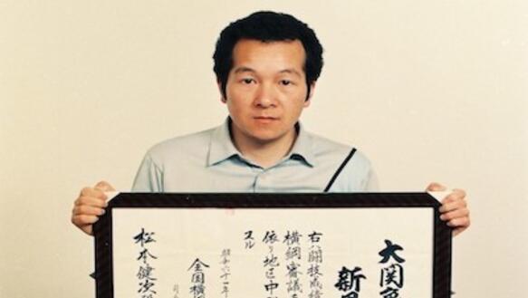 Porträtfoto von Matsumoto Kenji mit einer Zeichnung auf seinem Schoß